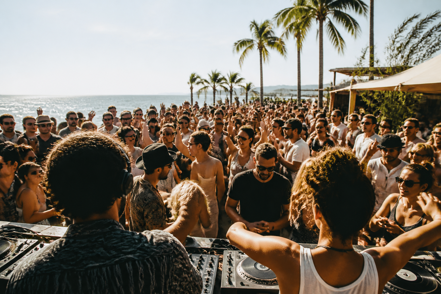 A sunlit coastal crowd dancing at an outdoor listening party